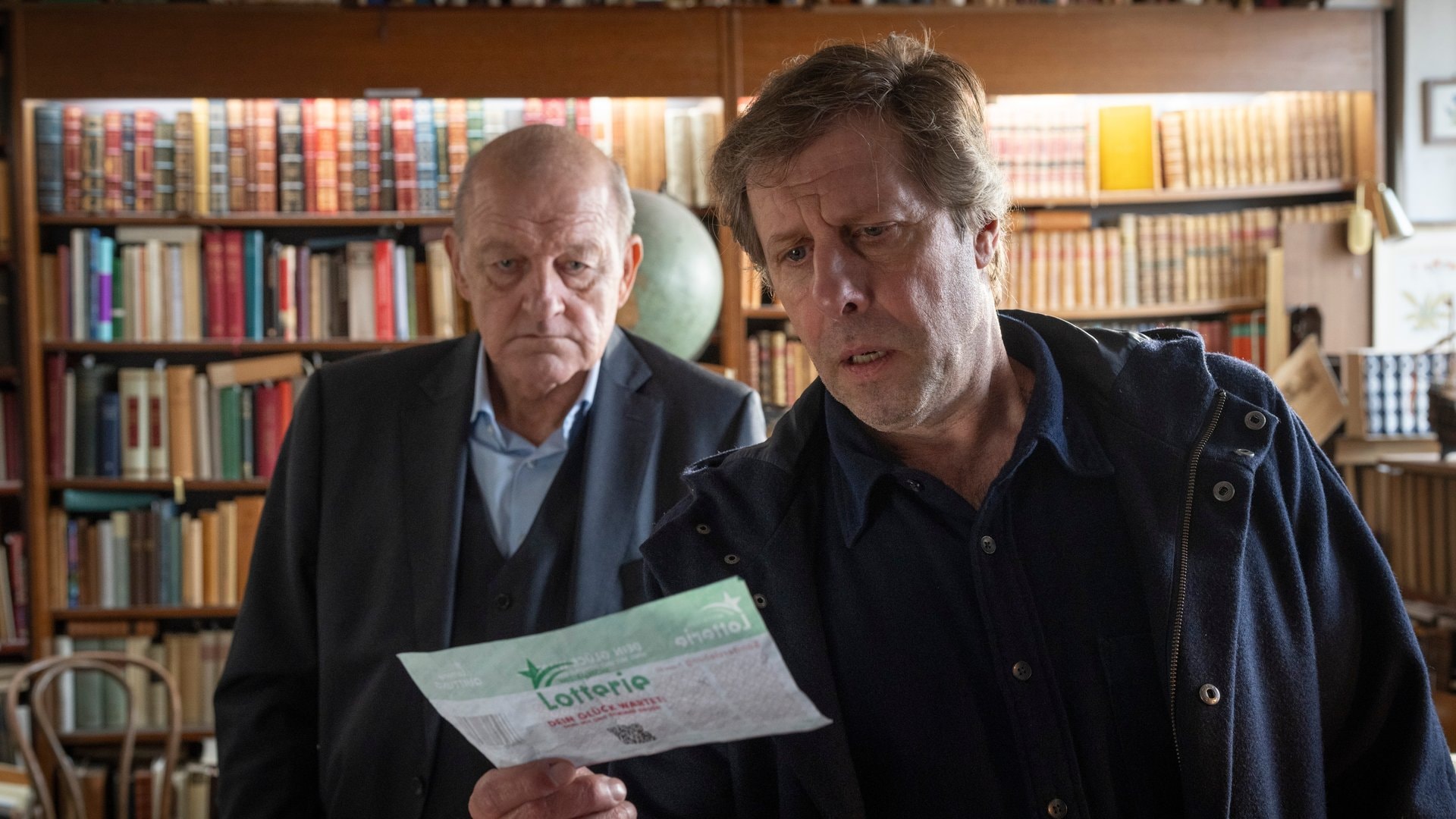 «Wilsberg: Todsicherer Tipp»: Privatdetektiv Georg Wilsberg (Leonard Lansink, l.) und Ekki Talkötter (Oliver Korittke) entdecken zwischen den Seiten eines alten Buches etwas Unerwartetes.